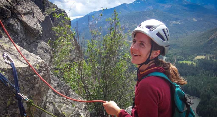 a person smiles as they hold a rope while rock climbing